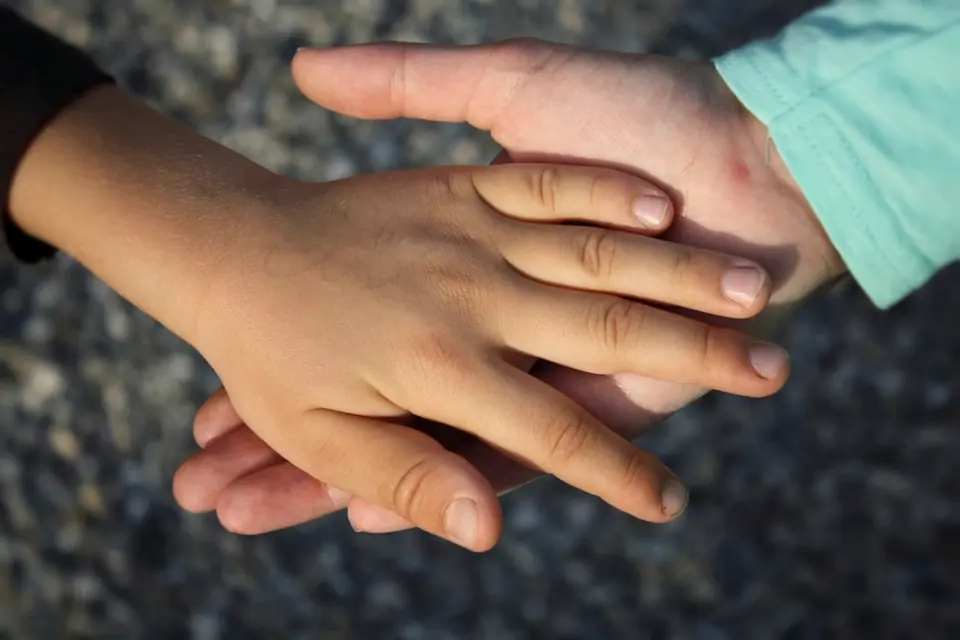 An adult's hand resting over a child's hand